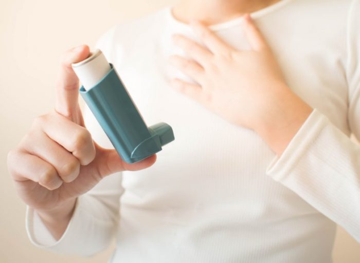 Man suffering from wheezing showing inhaler while placing his one hand on chest.
