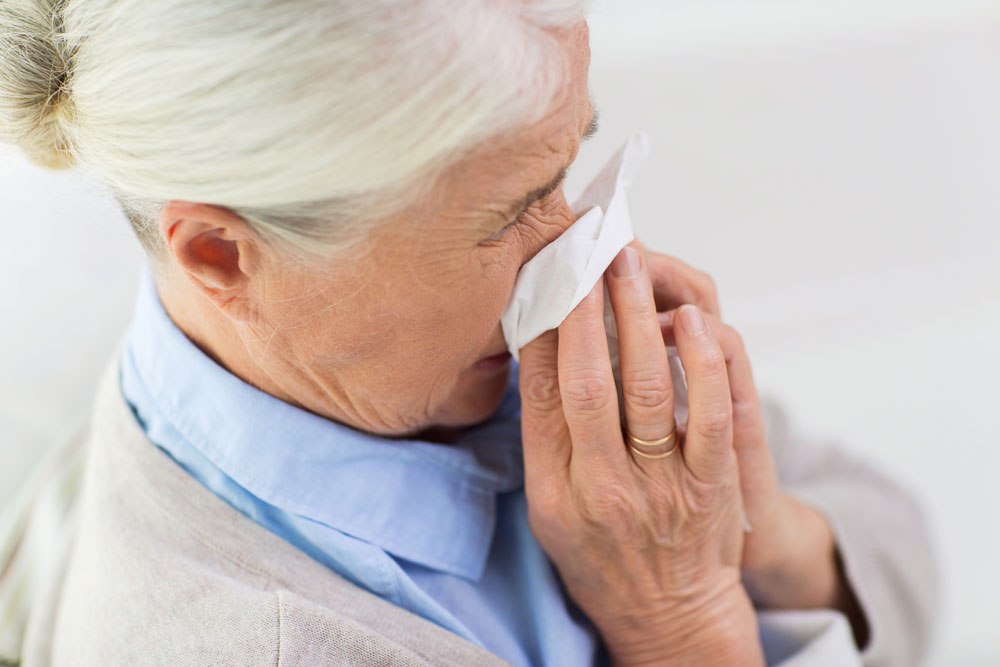 Sick senior woman blowing nose to paper napkin to protect herself and others from COVID-19