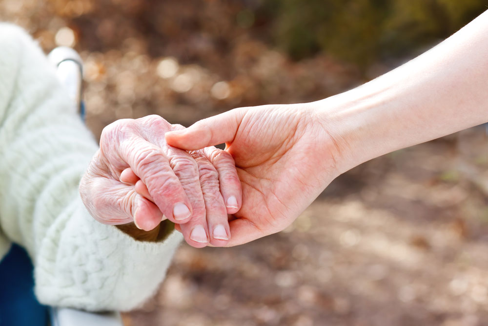 Senior lady suffering from extreme fatigue holding hand of young caretaker