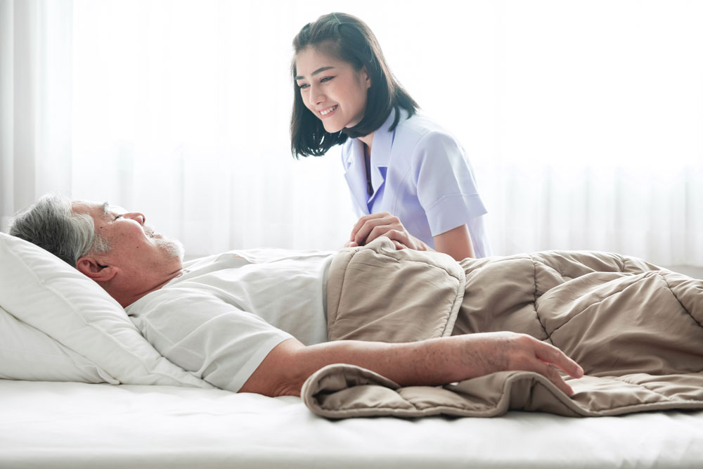 Senior man with pressure ulcers on bed and nurse waking him up