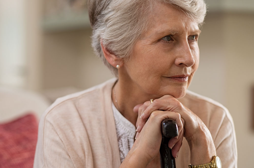 Senior woman suffering from memory loss sitting on couch holding walking stick