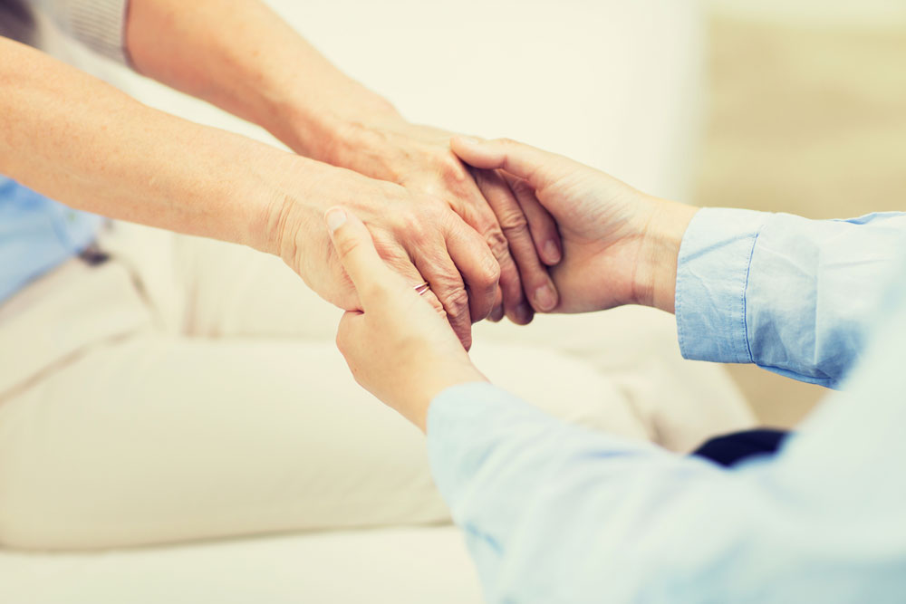 Nurse holding hands of an elderly woman and providing emotional support