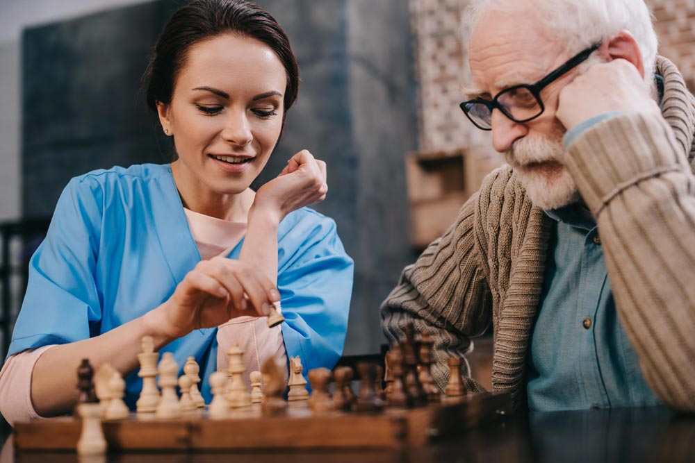 Elderly man playing chess with female nurse during brain exercises