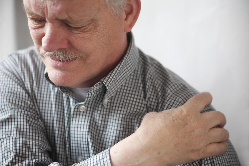 Elderly main holding his shoulder suffering from frozen shoulder