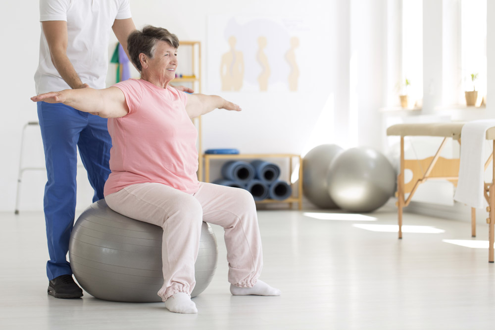Nurse helping elderly woman with balance exercises on a fit ball