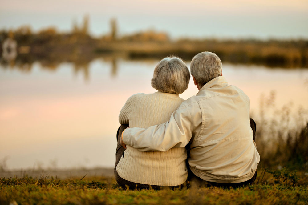 Elderly couple suffering from Parkinson's disease caring for each other and sitting next to a lake