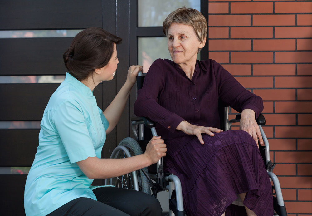 Nurse talking with a senior woman with limited mobility in joints sitting on a wheelchair