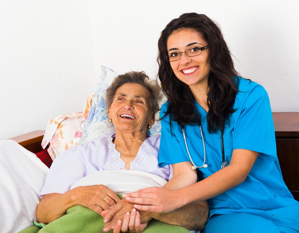 Nurse holding hands of an elderly woman lying on the bed and smiling to beat fatigue after surgery