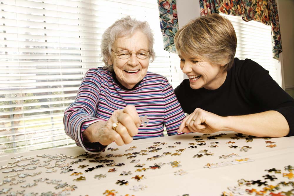 Elderly woman and younger woman doing puzzle activity as a part of recreation therapy to boost recovery.