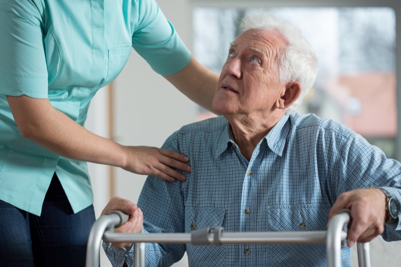 Nurse helping elderly man with the risk of infection to stand up using support