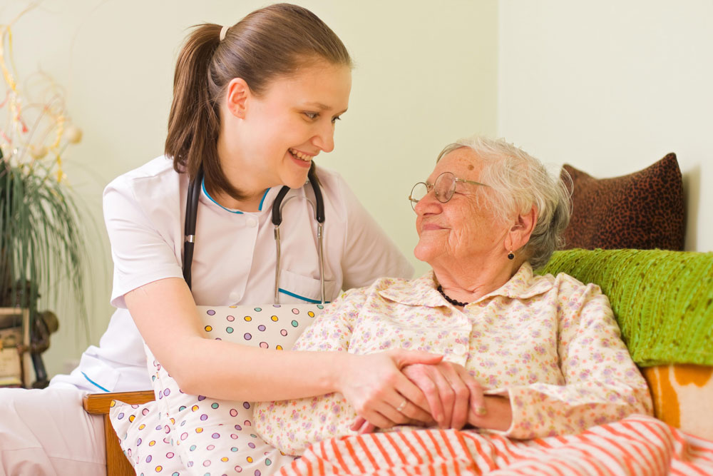 Nurse taking care of an elderly woman with right arm pain lying on bed during post-surgery recovery.