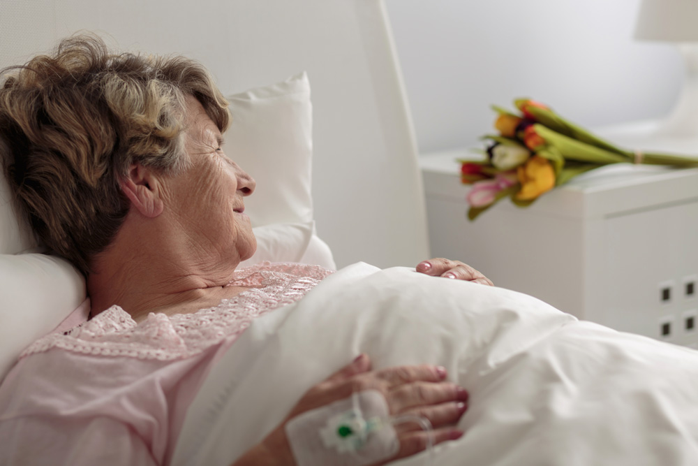 Senior woman with bed sores lying on bed and looking at tulip bouquet.