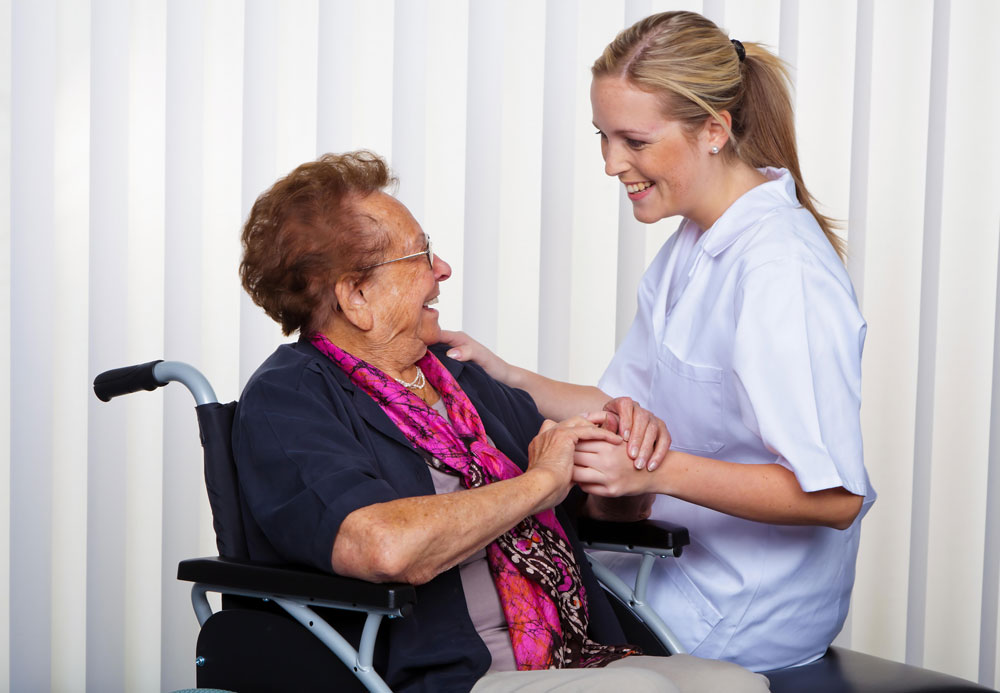 Happy senior woman going through amputation care during post-surgical syndrome sitting on a wheel chair and holding hands of a nurse.