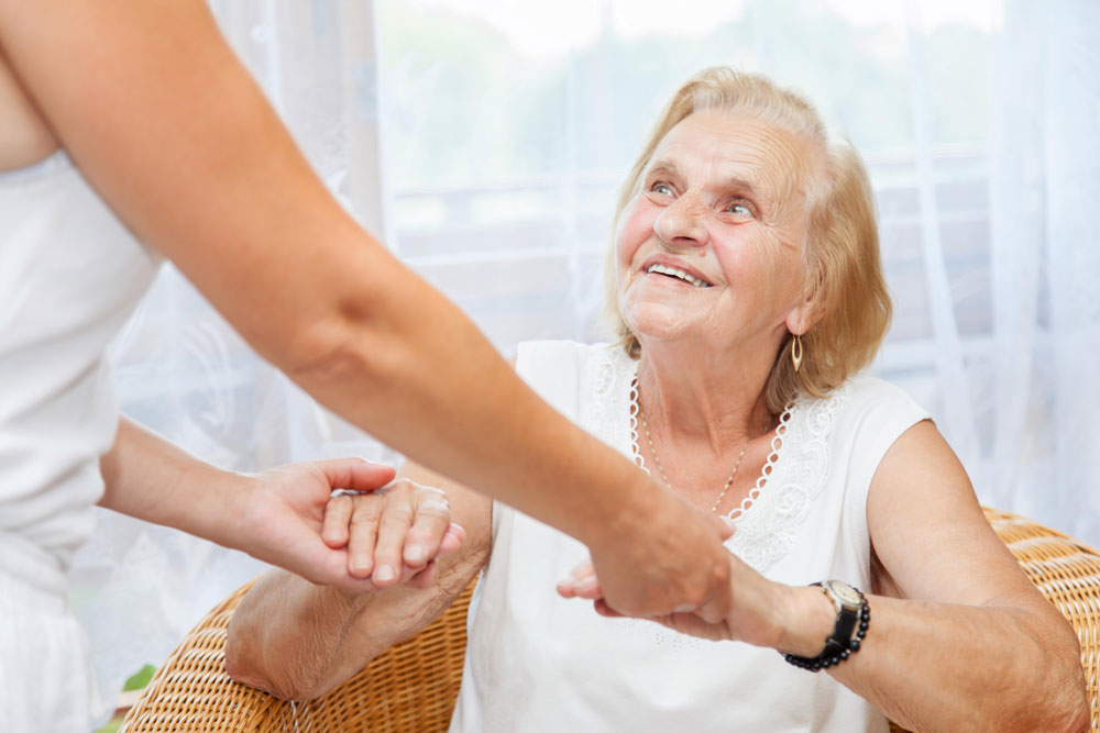 Nurse holding hands of a happy elderly woman who benefited from the advantages of rehab for neurological conditions.