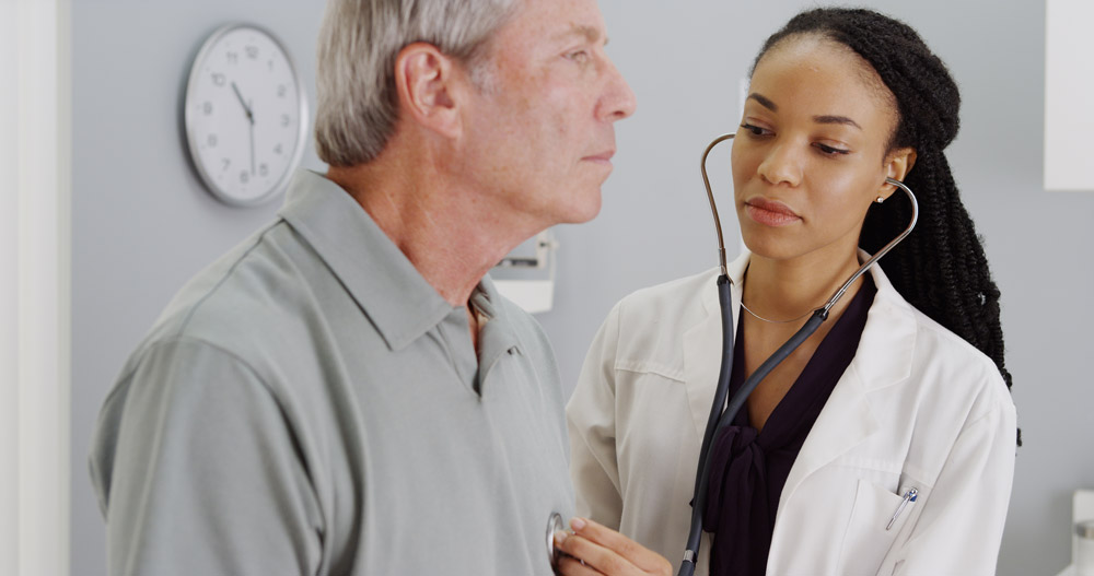 Female nurse using stethoscope to listen to the sounds produced by elderly mans' heart in order to diagnose septal infarct