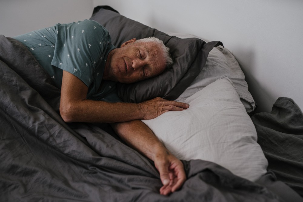 Senior man sleeping on his side in bed, illustrating poor sleep posture potentially causing neck pain.